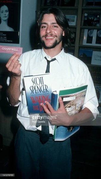 a man holding two books in his hands and smiling at the camera while wearing a tie