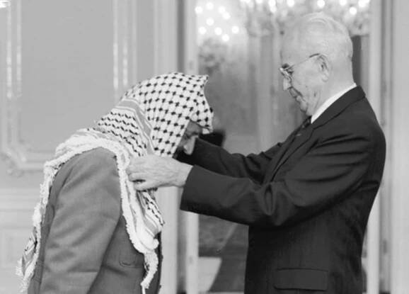 Návštěva Jásira Arafata v Praze, 18. října 1989. Do Československa tehdy přijel i Bassam Abu Sharif, podle amerického časopisu Time nejznámější tvář palestinského teroru. Prezident ČSSR Gustáv Husák (vpravo) předal na Pražském hradě předsedovi výkonného výboru OOP Jásiru Arafatovi Československý řád Bílého lva I. třídy.