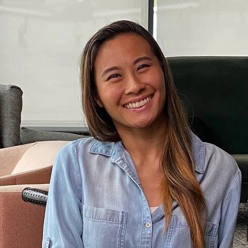 Michele  is smiling in an office setting. She is wearing a blue denim button up and her long hair is pushed to one side.