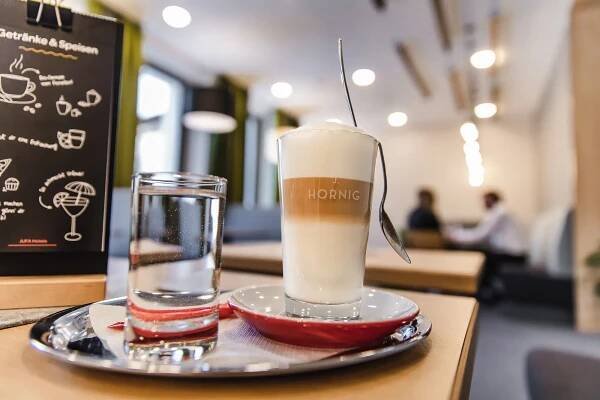 Ihr seht einen Latte Macchiato im gemütlichen Café im JUFA Hotel Schladming. Der Ort für erholsamen Familienurlaub und einen unvergesslichen Winterurlaub.