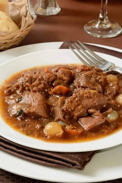 A plate of rich and savory boeuf bourguignon, a classic traditional French foods, featuring tender beef slow-cooked in red wine with onions, mushrooms, and carrots.