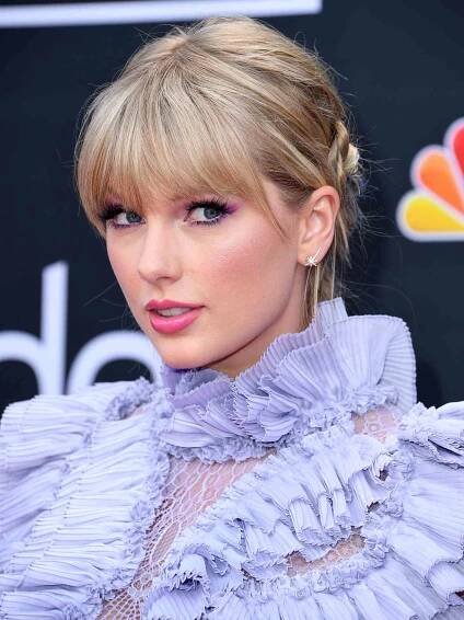 Taylor Swift with blonde, bucolic bangs while wearing a lavender gown with ruffles