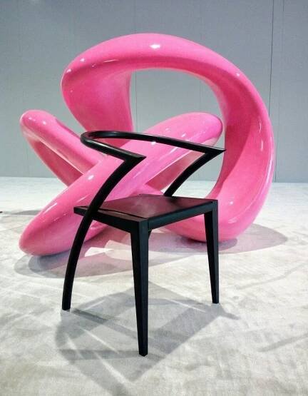 a pink chair sitting on top of a white floor next to a black chair and ottoman