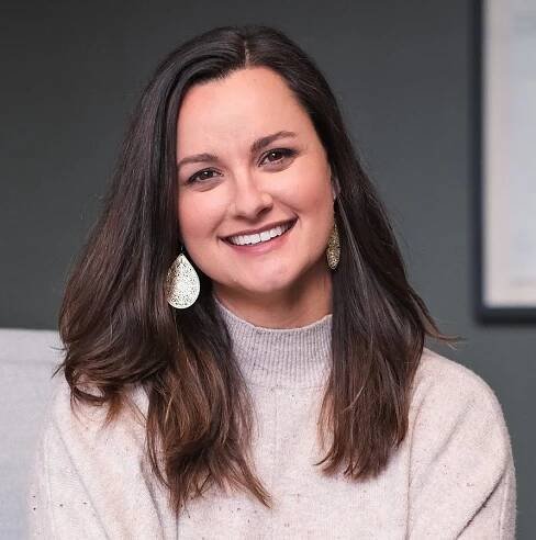 Smiling woman with teardrop earrings and beige sweater.
