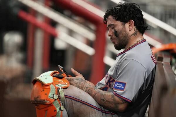 Francisco Alvarez, Mets player, on bench looking at phone.