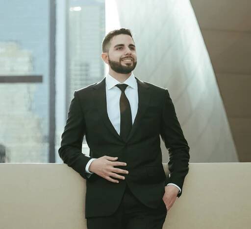 Jon Sargsyan, a partner at the Injury Law Firm, LLP, wearing a black suit and tie in front of city buildings in Los Angeles