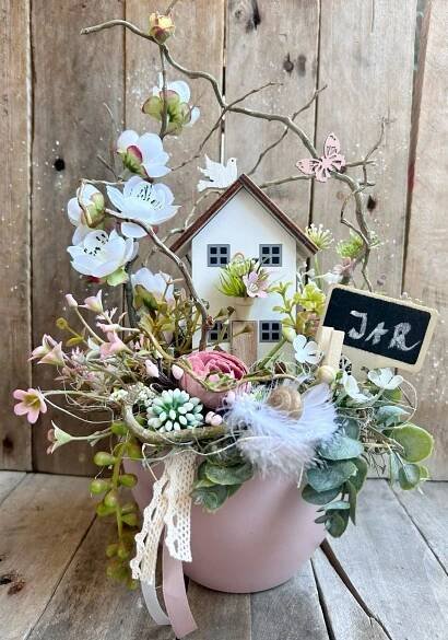 a potted plant with flowers and a birdhouse in it sitting on a wooden table