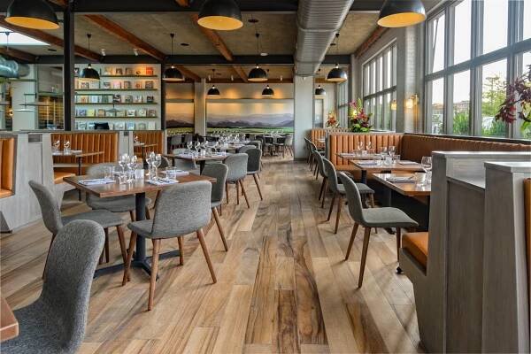 The dining room at Redd Rochester restaurant in NY with wooden floors, an exposed ceiling and a wall of windows