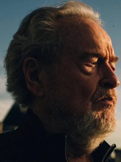 A close-up portrait shows a pensive Ridley Scott bathed in golden light. He has a beard and his hair is blowing back slightly.