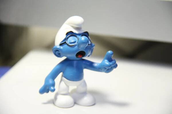 Brainy Smurf in white hat and pants and round glasses, eyes closed while finger pointing in front