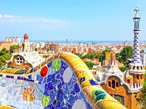Barevná mozaiková lavička v parku Güell s výhledem na panorama Barcelony s výraznou architekturou a vzdáleným výhledem na moře.