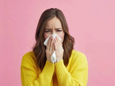 A woman sneezes into a tissue requires hay fever treatment for her symptoms