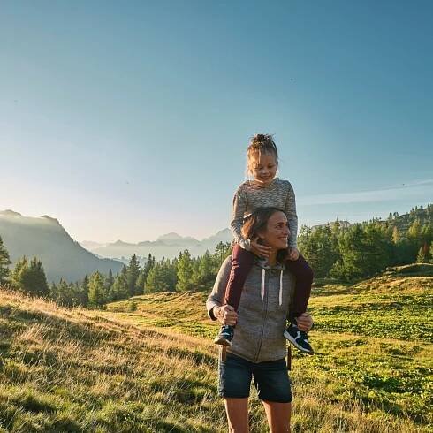 Mom carrying her daughter on her shoulders on a lawn land near Falkensteiner Hotels & Residences