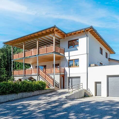 Modernes WOLF Haus mit nachhaltiger Bauweise, zweistöckig mit Holzveranda und großen Fenstern, umgeben von Natur.