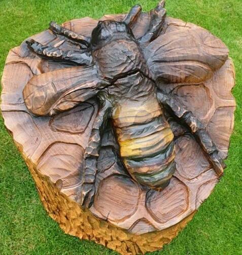 a statue of a bee sitting on top of a wooden stump in the middle of grass