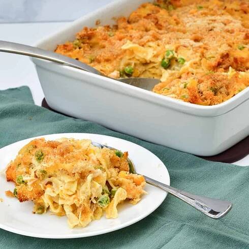 chicken noodle casserole on a white plate on a green napkin next to a white casserole dish fished with more casserole