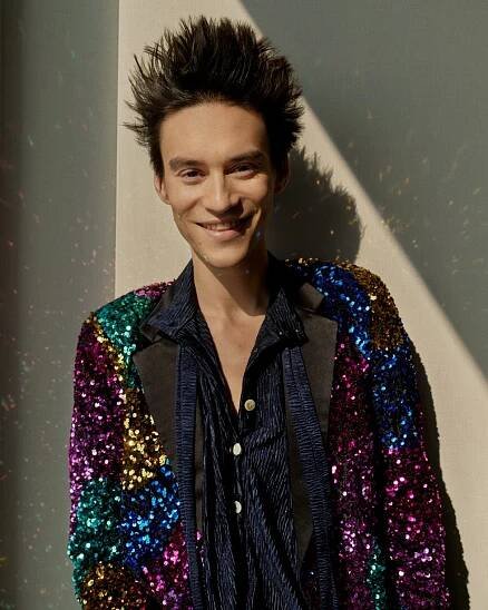 person wearing a colorful sequined jacket against a neutral background