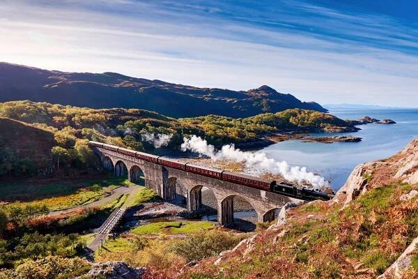 The Jacobite Steam Train and seven carriages cross a viaduct in Scotland. A rail trip in the Scottish Highlands is one of the best trips of a lifetime