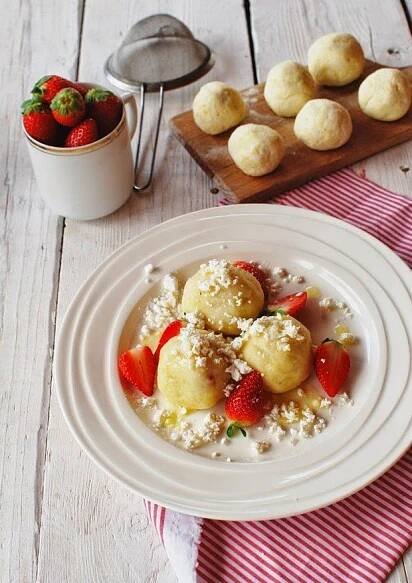 a white plate topped with fruit covered dessert next to a bowl of strawberries and muffins
