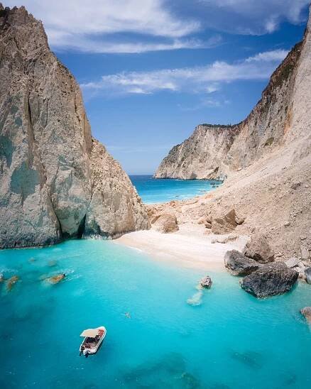A white sand beach surrounded by turquoise blue water at Mizithres Beach in Zakynthos Island, a small boat floating just off shore