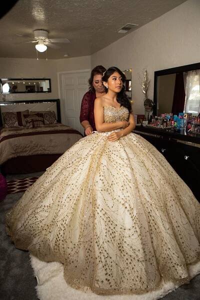 A stunning champagne-colored ballgown with intricate beading and full skirt photographed in a bedroom.