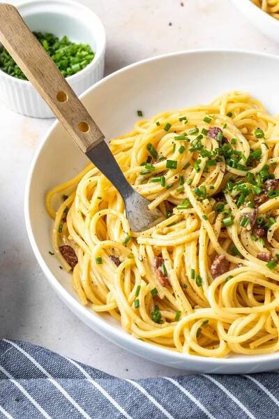 Close up of creamy pasta carbonara in a bowl with a fork. 