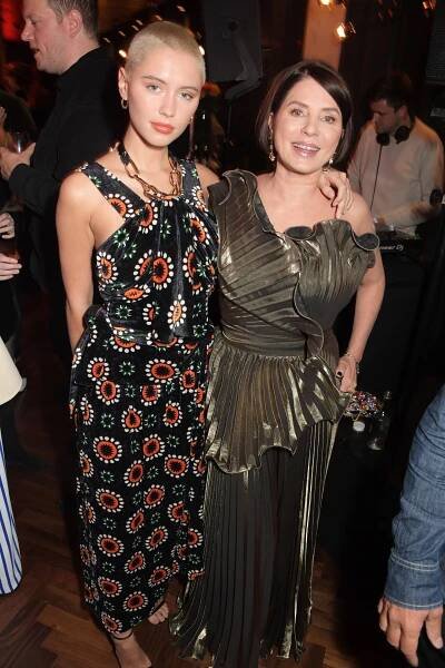 a woman in a pleated dress stands next to a woman with a shaved head