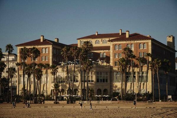 Exterior shot of Casa del Mar Hotel taken from the beach, displaying palm trees and humans walking