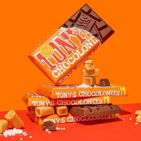 Four chocolate bars placed on top of each other, one propped up by pieces of small chocolate on an orange background