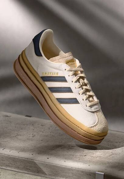 Tenisky Adidas Gazelle s krémovým semišovým svrškem, modrými koženými detaily, třemi modrými pruhy, béžovou mezipodešví a hnědou gumovou podešví.