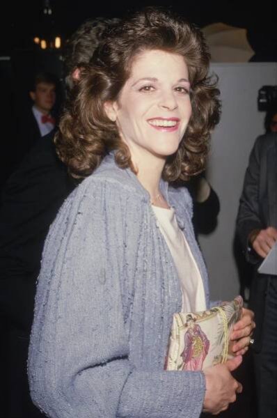 Circa 1982 candid portrait of actor and comedian Gilda Radner smiling and holding a purse with an Asian design