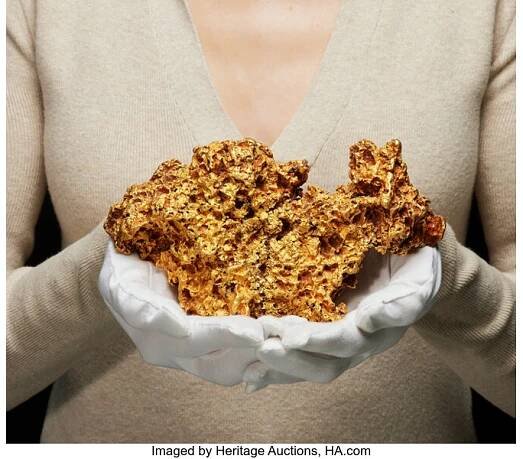 a woman with white gloved hands holds a large golden nugget