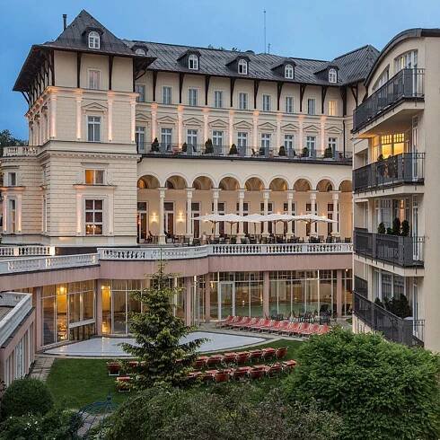 Luxusní hotel s vnitřním dvorem, bazénem a lehátky v zahradě, lemované stromy a keři.