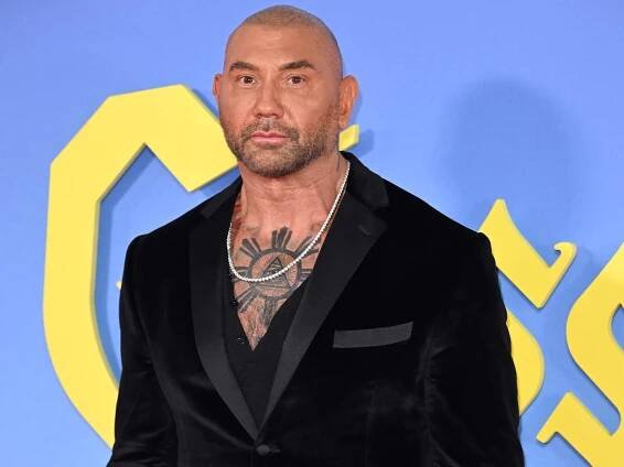 Dave Bautista in a black suit showing his chest tattoo
