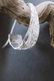 Earring with texture of a web is hanging on a driftwood