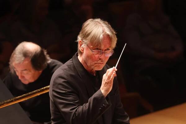 Man with white hair and glasses holding a conductor's wand