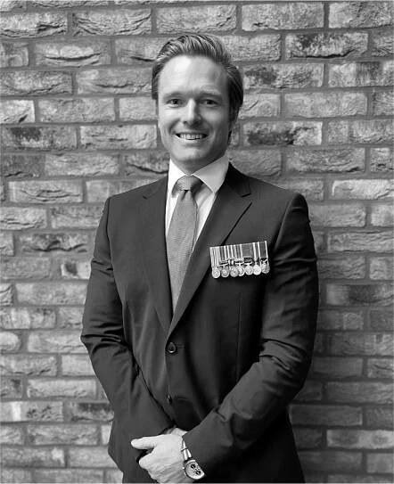 Picture of Nathan Jones smiling and looking into the camera. He is wearing a suit with medals pinned to the pocket.