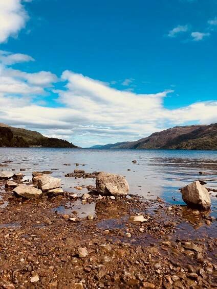 bezplatná Klidné pobřeží jezera Loch Ness s jasnou oblohou a vzdálenými kopci ve Skotské vysočině. Základová fotografie