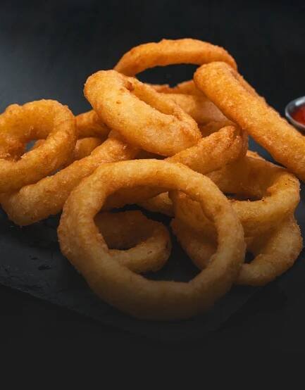 A pile of onion rings with ketchup on a black plate.