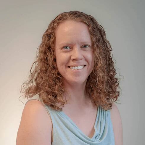 A woman with curly hair is smiling and wearing a blue tank top.