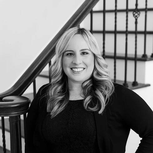 A black and white photo of a woman standing next to a staircase.