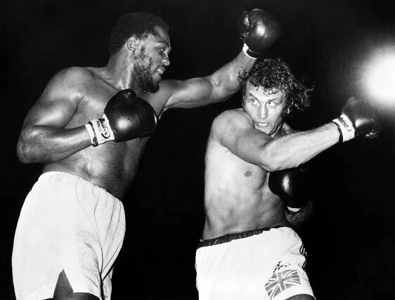Black and white photo of Joe Frazier and Joe Bugner boxing.
