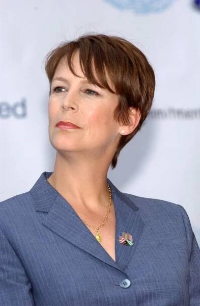 Jamie Lee Curtis delivers a poised appearance at the launch of Ford’s Blue Oval Certified Commitment to Kids program, wearing a sharp pinstripe suit and gold pendant, with an American flag pin adding a patriotic touch.