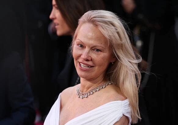 Pamela Anderson smiling at the camera, attending the 2025 British Academy of Film and Television Awards at the Royal Festival Hall in London