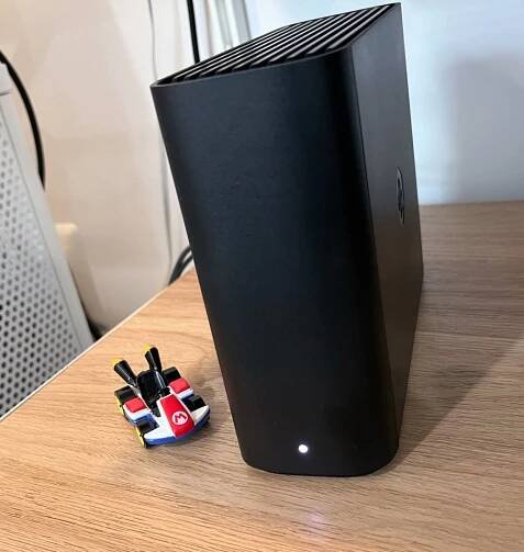 A black rectangular slab standing up, on a faux-wood shelf, next to a Mario Kart figurine.