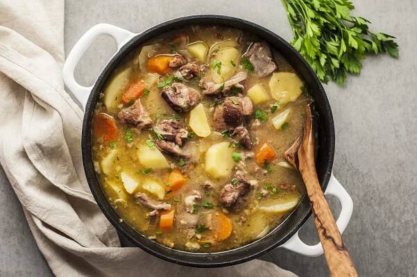 Traditional Irish lamb stew with vegetables in a Dutch oven with a rustic wooden spoon in the pot and sprigs of parsley nearby