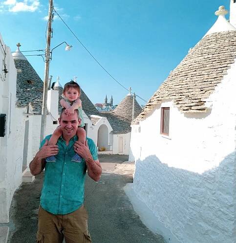 toddler on father's shoulders in front of white trulli, alberobello