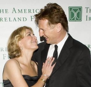 Natasha Richardson rests her hand on Liam Neeson's chest and looks up at him.