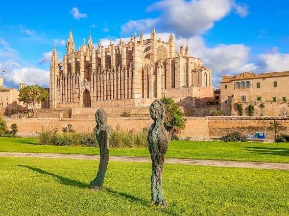 2 bronze sculptures a the foreground and a beautiful cathedral at the background; the Cathedral of Mallorca as seen from Parc de la Mar in Palma