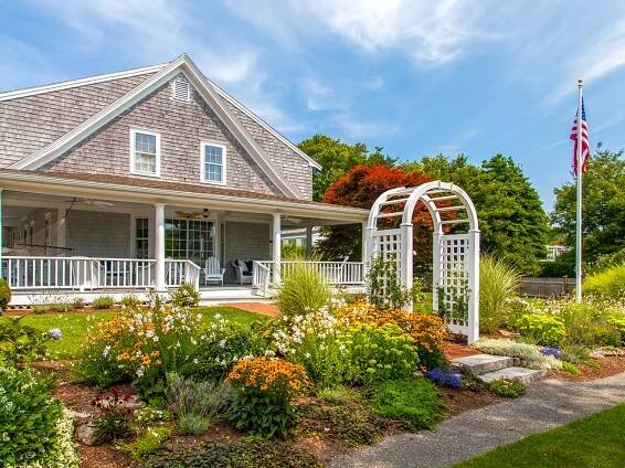 White arbor in front of a yard full of flowers, with a flagpole to the right